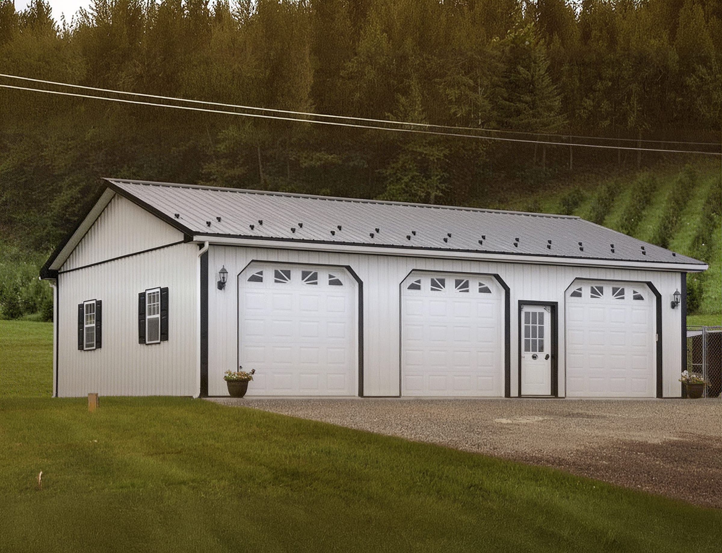 A finished white post-frame garage with three overhead doors and black trim on a wooded Delaware property.